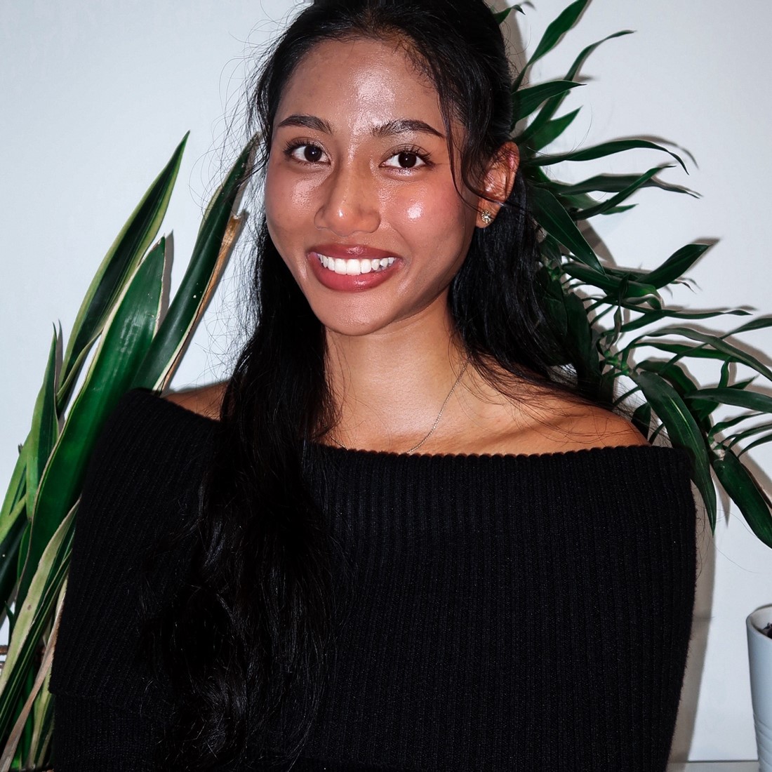 Nathida smiling, standing in front of a plant