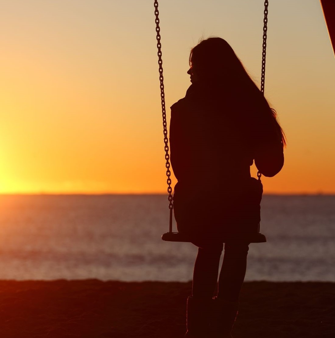 Girl on swing looking out to sunset