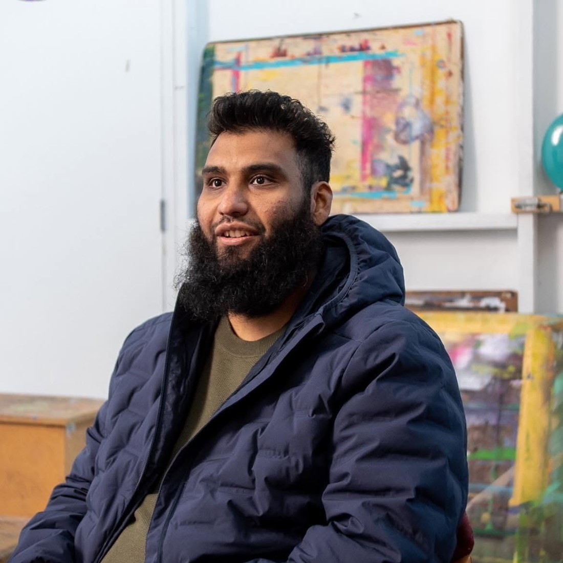 Annas, the guest on this episode of the podcast, sitting in a room smiling, with various paintings behind him.