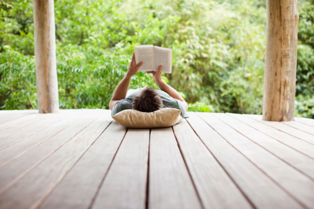 Man lying down reading book on porch