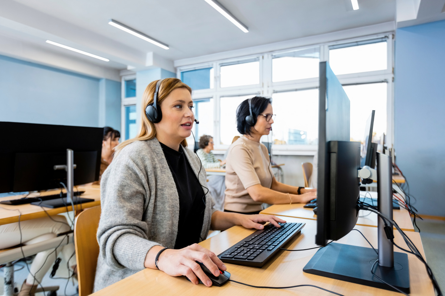Two women sitting at computers at a call centre, talking into headset microphones.