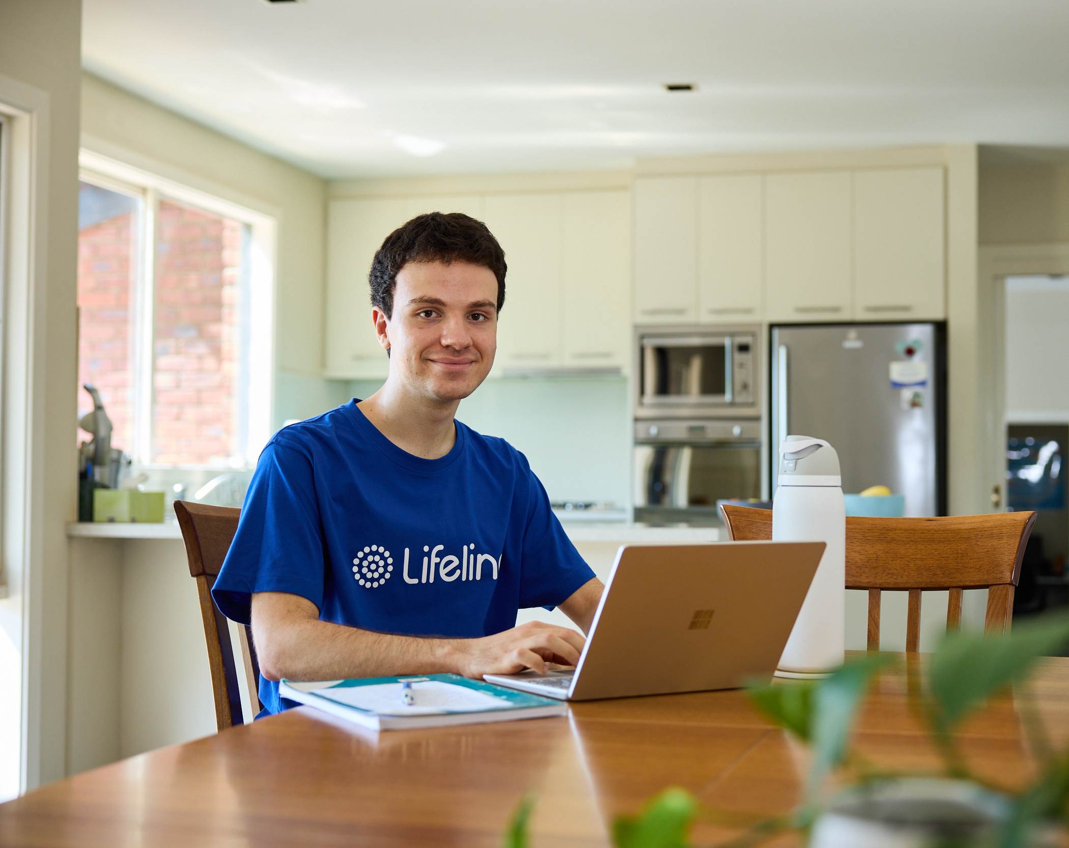 Young male Lifeline crisis supporter sitting with laptop at kitchen table