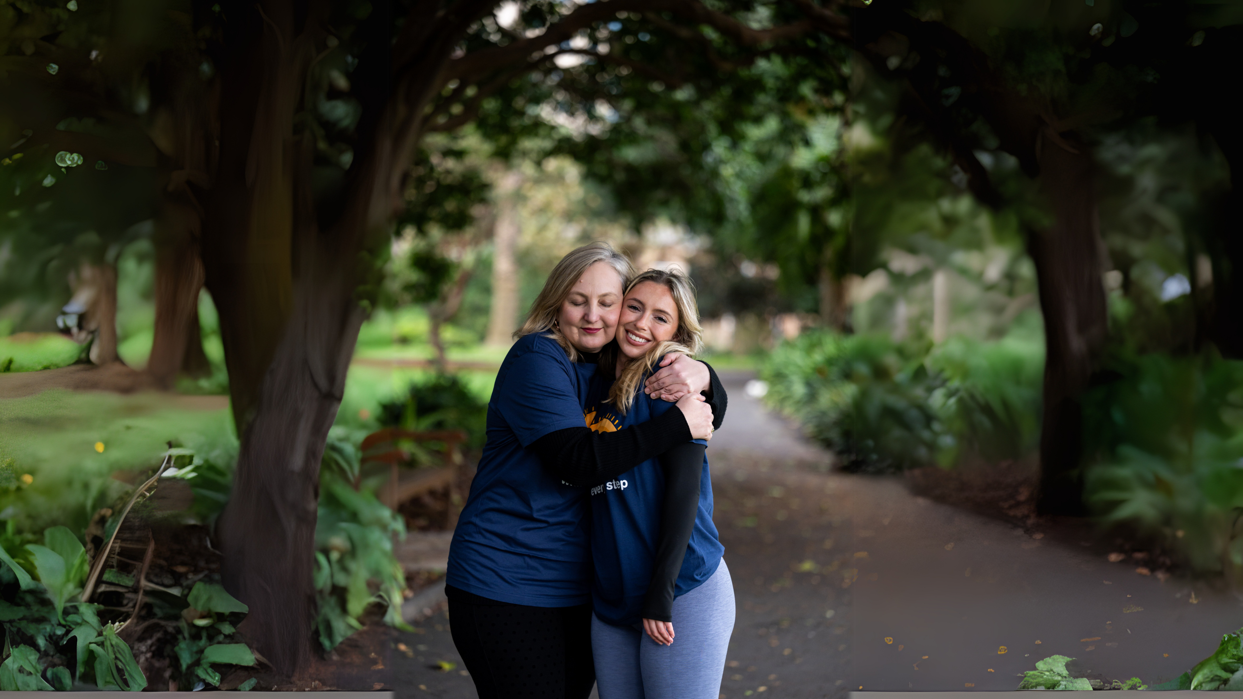 Two women, volunteering for Lifeline's 'Out Of The Shadows' event, hugging in a park.