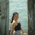 Yasmin smiling while sitting on a wharf beside the water, framed between two weathered timber posts.