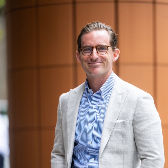 Luke Damon, wearing a tan sportscoat, standing on the steps of an office building in Sydney CBD
