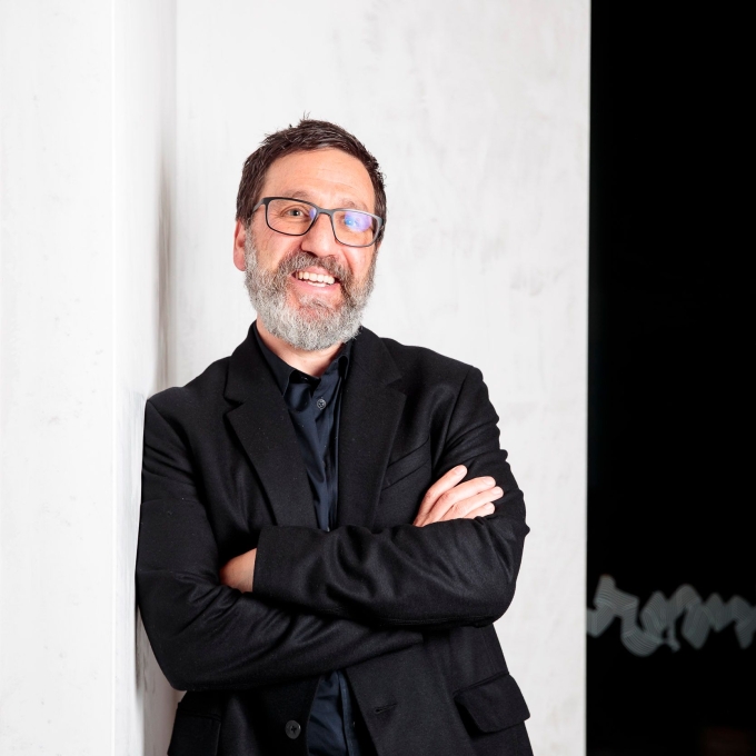 Dr Tim Sharp smiling with his arms crossed, wearing glasses and a black suit.